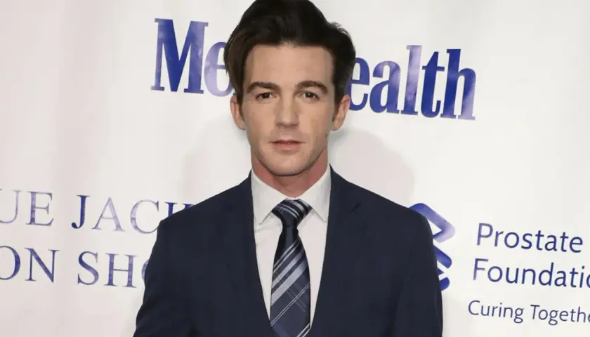 Drake Bell w garniturze, znany z filmów, seriali i programów, pozuje na tle wydarzenia charytatywnego.