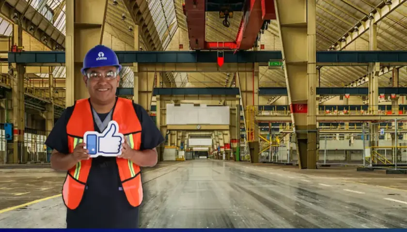 Hombre con casco y chaleco naranja sonríe en una nave industrial, sosteniendo un pulgar hacia arriba. Sus sistemas de limpieza son eficientes.