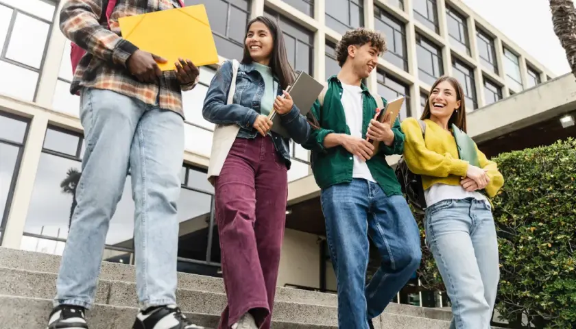 Grupa studentów schodzi po schodach, niosąc książki i teczki. Ich uśmiechy sugerują, że są gotowi na wyzwania, niczym w ramach obrony cywilnej.