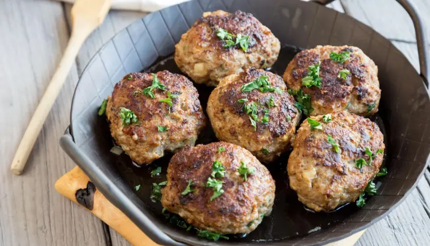 Sechs goldbraune Fleischpflanzerl, garniert mit Petersilie, in einer Pfanne. Ein leckeres Fleischpflanzerl Rezept zum Nachkochen.