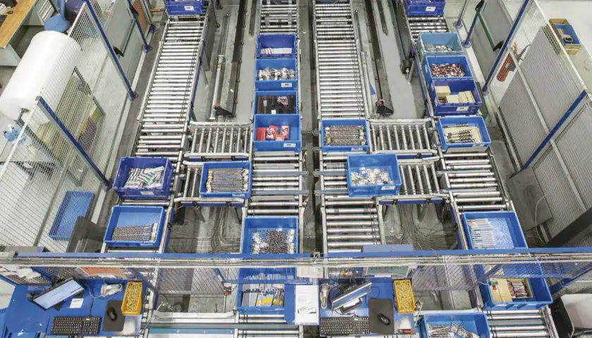 Ein Lager mit Rollenbahnen und blauen Behältern, die Werkzeuge und Materialien enthalten. Dies zeigt die Effizienz und Organisation, die durch Kanban-Vorteile erreicht werden.