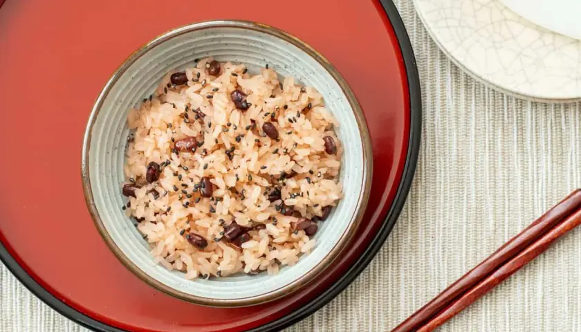 A bowl of Japanese red bean rice, sprinkled with black sesame seeds, sits on a red tray.