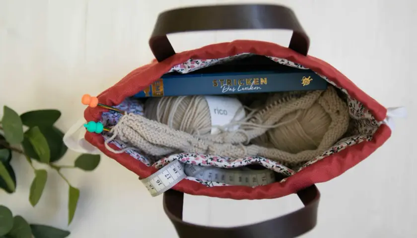 Kreative Ideen für upcycling taschen selber machen: Wolle, Stricknadeln, ein Buch und Maßband in einer roten Tasche.