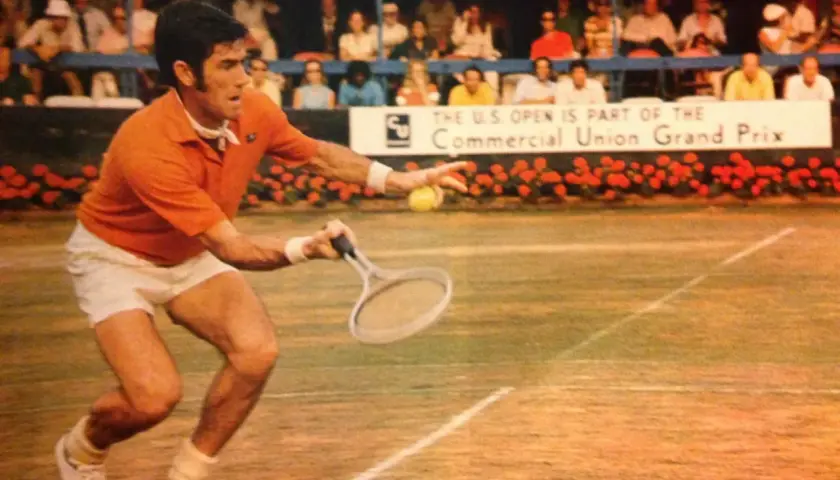 Ken Rosewall w akcji na korcie, w pomarańczowej koszulce i białych spodenkach, podczas meczu U.S. Open.