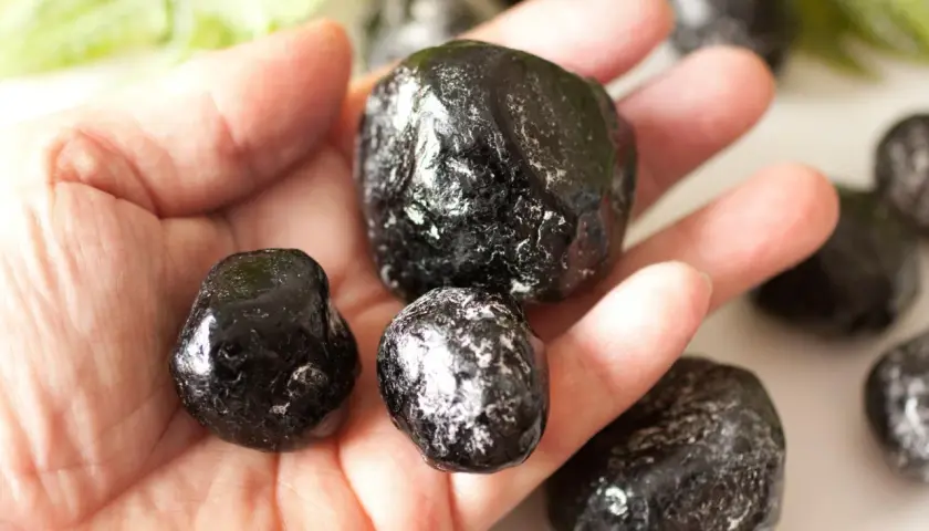 Eine Hand hält mehrere glänzende, schwarze Apachentränen-Steine. Sie sehen aus wie kleine, dunkle Tropfen.