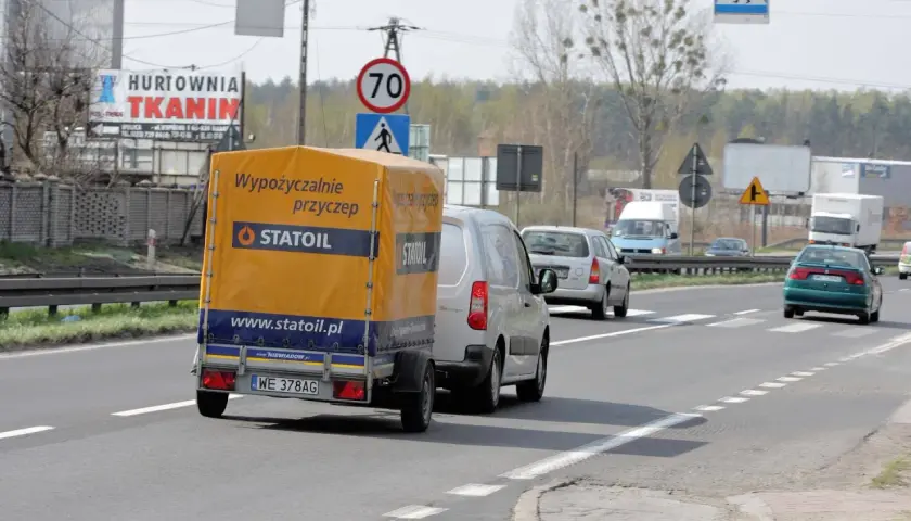 Na drodze widać przyczepę z napisem "Wypożyczalnie przyczep Statoil". Znak ograniczenia prędkości wskazuje 70 km/h, co sugeruje, ile autobus może jechać na autostradzie w takich warunkach.