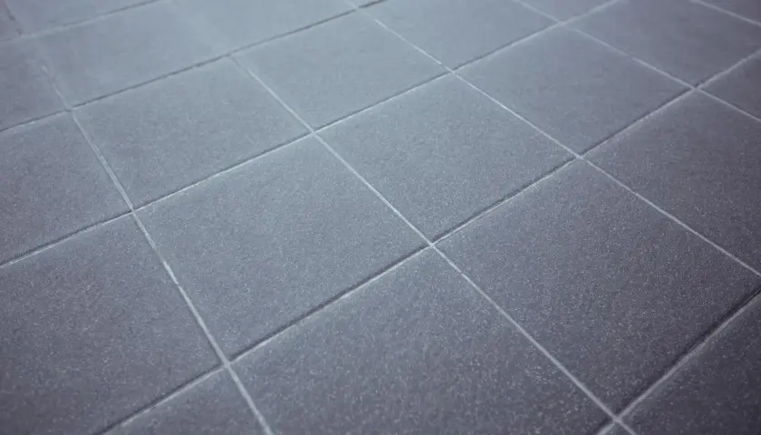 Dettaglio di piastrelle grigie con fughe pavimento pulite e uniformi, che creano un motivo geometrico ordinato.