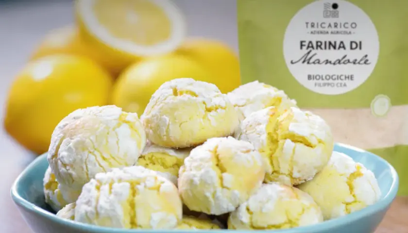 Biscotti con farina di mandorle, morbidi e profumati, accanto a limoni freschi e una confezione di farina.