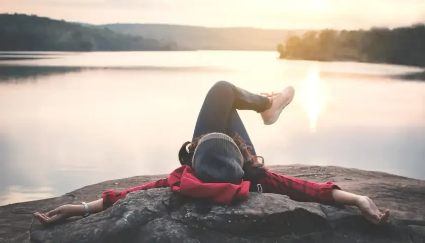Kobieta odpoczywa na skale nad jeziorem, ciesząc się spokojem. To idealny moment na dodatkowy urlop i relaks.