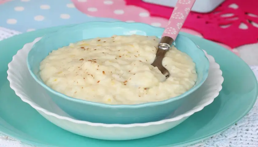 Un cremoso riso e latte, cosparso di cannella, servito in una ciotola azzurra con un cucchiaino rosa.