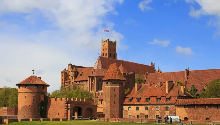 Potężny zamek z czerwonej cegły, z wieżami i czerwonymi dachami, góruje nad zielonym trawnikiem. To najpiękniejszy zamek w Polsce, duma historii.