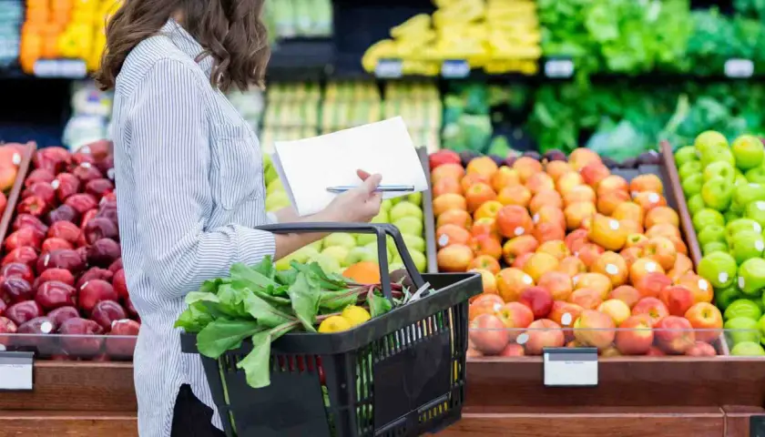 Donna con lista della spesa sceglie verdure fresche e frutta colorata al supermercato.