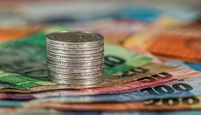Stos monet na tle kolorowych banknotów.