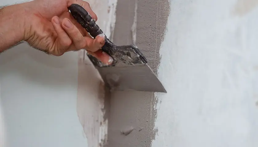 Mano con spatola applica stucco per riparare una crepa nel muro. Ottime idee per coprire una crepa nel muro con finitura liscia.