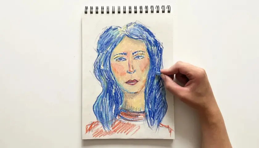 Portret kobiety z niebieskimi włosami, tworzony pastelami. Ręka dodaje ostatnie pociągnięcia, tworząc efekt dragana.