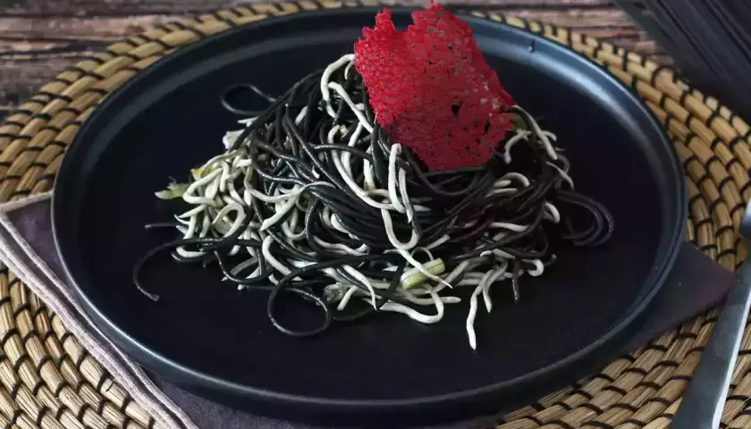 Spaghetti neri e bianchi, un contrasto elegante. Il nero di seppia dona un sapore unico a questo piatto, guarnito con una cialda rossa croccante.