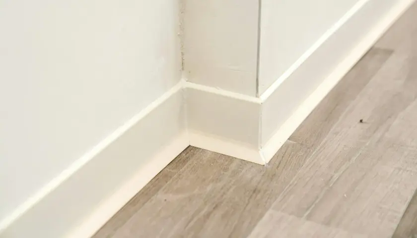 Angolo di un battiscopa in ceramica bianca, pronto per essere incollato su un pavimento in laminato grigio.