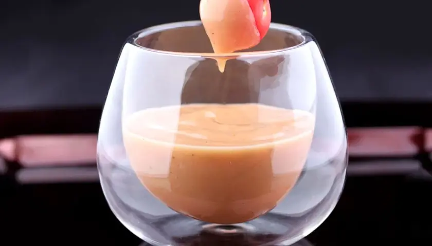 Une tomate cerise trempée dans une sauce cocktail onctueuse, servie dans un verre élégant.