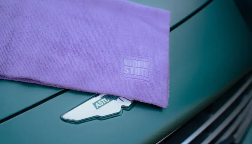 Fioletowy ręcznik z mikrofibry z logo Work Stuff leży na zielonym samochodzie Aston Martin. Dowiedz się, jak prać ręcznik z mikrofibry, by służył latami.