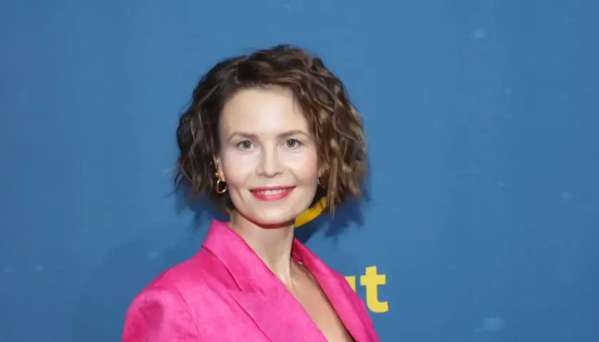 Magdalena Kumorek w różowej marynarce, uśmiechnięta na tle niebieskiego baneru.
