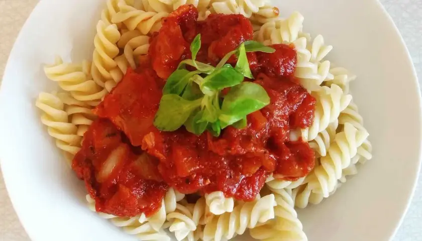 Fusilli con la mejor salsa de tomate italiana, cubierta con una hoja verde fresca.
