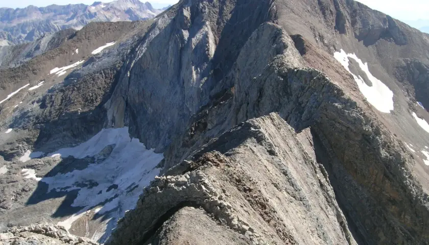 Cresta rocosa y escarpada, con restos de nieve, que se asemeja a un pico espadas en la inmensidad de las montañas.