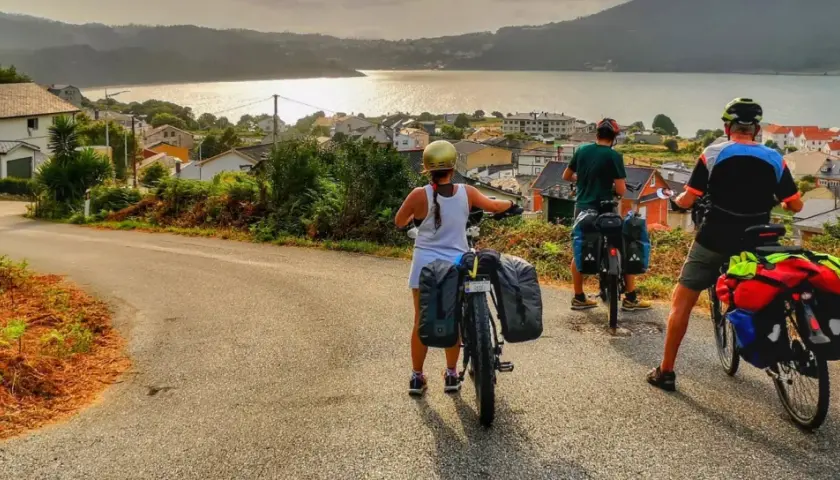 Ciclistas con alforjas exploran **rutas bicicleta** con vistas a un pueblo costero y el mar al atardecer.
