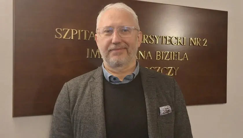 Mężczyzna w okularach i marynarce stoi przed tablicą z napisem "SZPITAL UNIWERSYTECKI NR 2 IM. JANA BIZIELA BYDGOSZCZ".