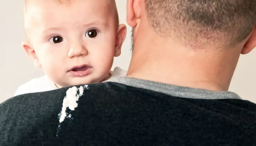 Un neonato di 1 mese ha un rigurgito, lasciando una macchia sul maglione del padre.