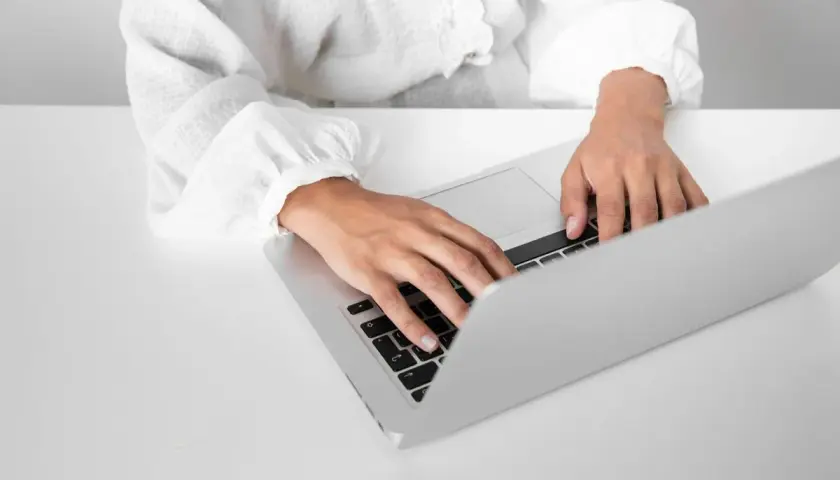 Dłonie piszą na laptopie, przygotowując zaświadczenie o niezaleganiu.