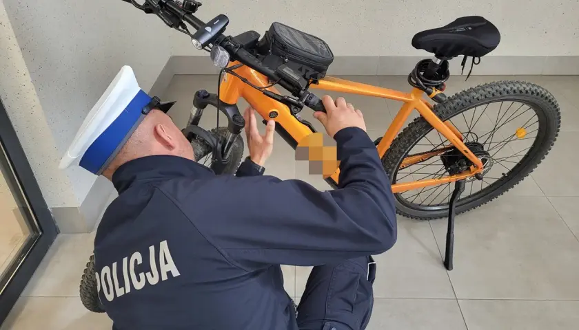 Policjant w czapce bada pomarańczowy rower elektryczny, próbując zrozumieć, jak działa rower elektryczny.