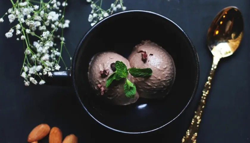 Deux boules de glace à la figue, garnies de menthe fraîche, dans un bol noir, avec des amandes et une cuillère dorée.