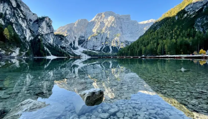 Der Pragser Wildsee spiegelt majestätische Berge und grüne Wälder. Kleine Boote liegen am Ufer.