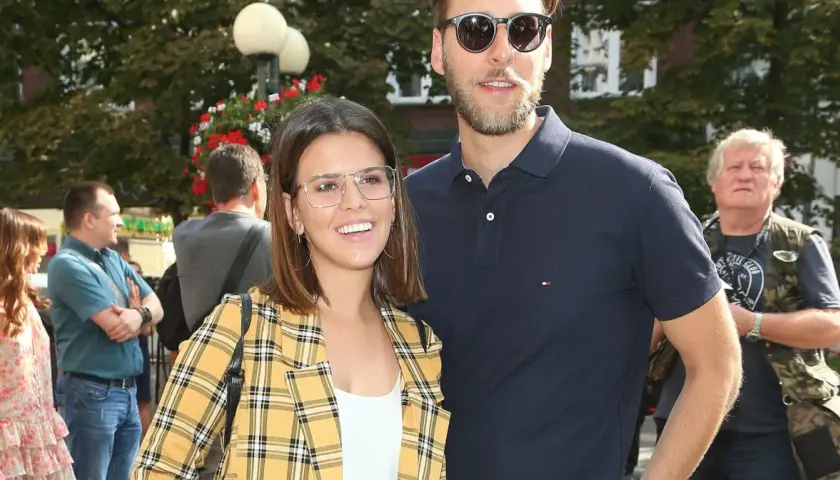 Monika Sawka z mężem, uśmiechnięci, w okularach, na tle drzew i ludzi.