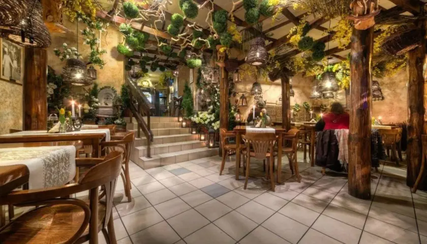 Przytulne wnętrze z drewnianymi meblami i bogatą roślinnością, idealne na romantyczną kolację. Polecane restauracje Katowice.