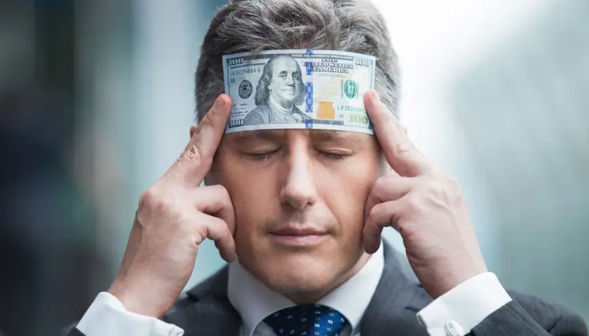 Biznesmen z banknotem 100 dolarów na czole, zamyślony nad tym, jak pomnażać pieniądze.