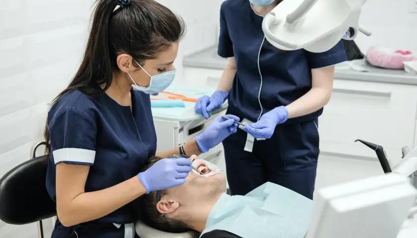 Dentystka w maseczce i rękawiczkach bada pacjenta. Czy u dentysty trzeba mieć maseczkę? Tak, dla bezpieczeństwa wszystkich.