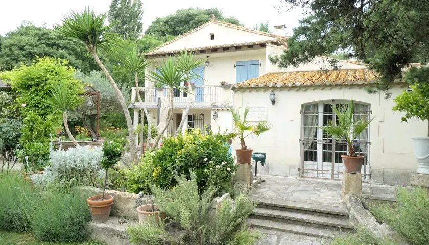 Maison en pierre avec jardin luxuriant, palmiers et lavande. Le panneau "Domaine des chênes truffiers" est visible.
