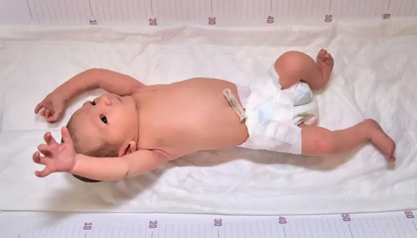 Neonato con pannolino e clip ombelicale, con le braccia sollevate, mostra i suoi riflessi neonatali su un telo con misurazioni.