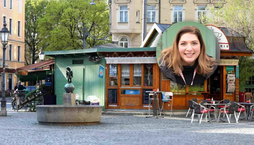 Lächelnde Frau vor einem Stehcafé in Haidhausen. Ein Brunnen und ein kleiner Junge als Statue sind im Vordergrund.