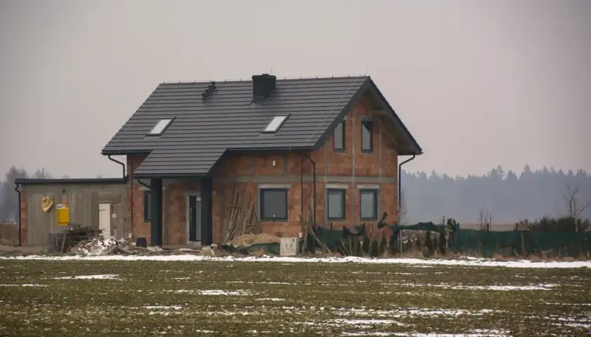 Dom w budowie, gdzie sprawdzić pozwolenie na budowę? Na placu budowy widać dom z cegły, dach i okna.