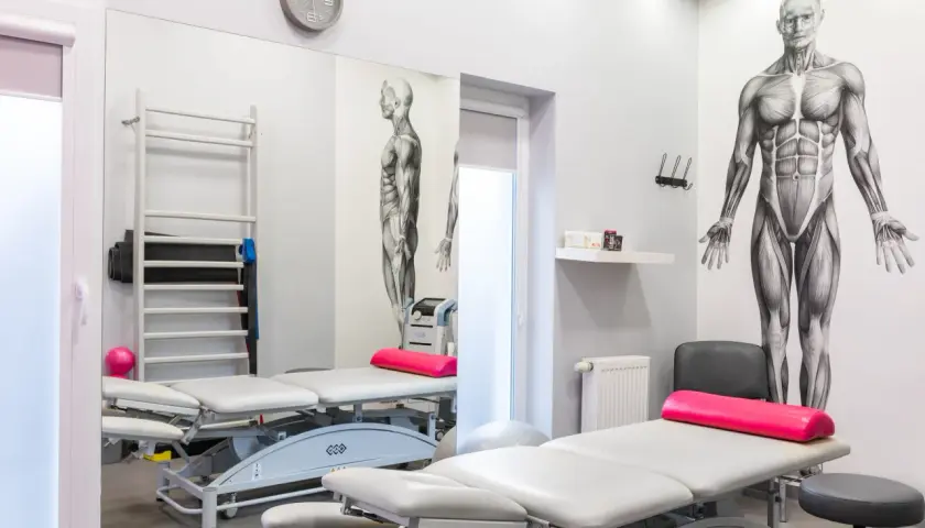 Gabinet fizjoterapii z łóżkami, drabinką, piłką i aparaturą do terapii polem magnetycznym.