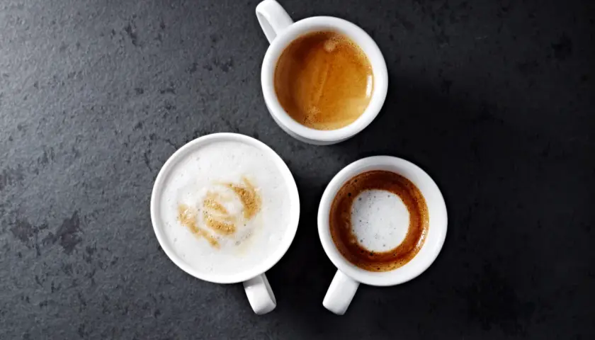 Trzy białe filiżanki z kawą: espresso, latte z wzorem i czarne espresso. Idealny poranek z parzeniem kawy.