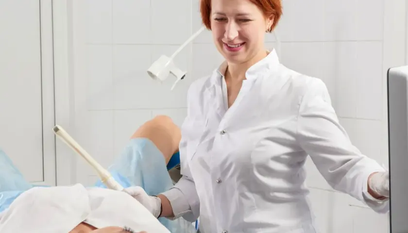 Lekarka bada pacjentkę, która leży na fotelu ginekologicznym. Specjalistka używa sondy USG, by zdiagnozować problemy, takie jak grzybica pochwy.