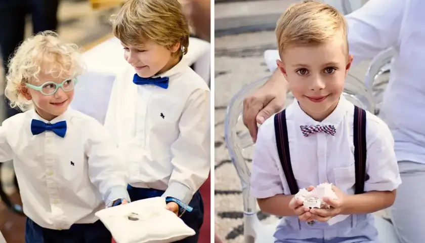 Uśmiechnięci chłopcy w eleganckich strojach, pełni powagi, niosące obrączki do ślubu. Jeden z nich ma okulary, drugi trzyma poduszkę z obrączkami.
