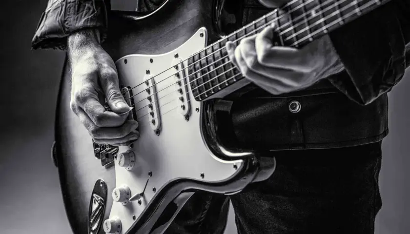 Dłoń gra na gitarze elektrycznej, ukazując klasyczne **marki gitar elektrycznych**.