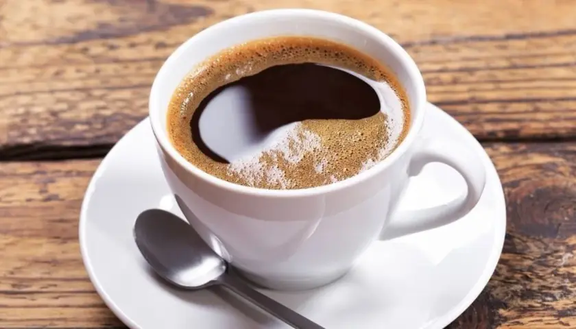 Aromatic coffee in a white cup, perfect for learning jak dobrze zaparzyć kawę sypaną. Na drewnianym blacie leży łyżeczka.