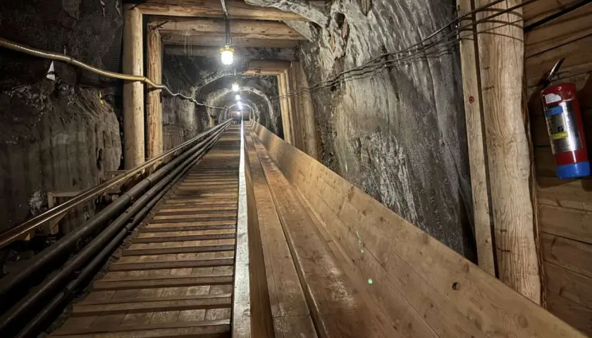 Długi, drewniany tunel w kopalni w Krakowie, oświetlony lampami, prowadzi w głąb ziemi.
