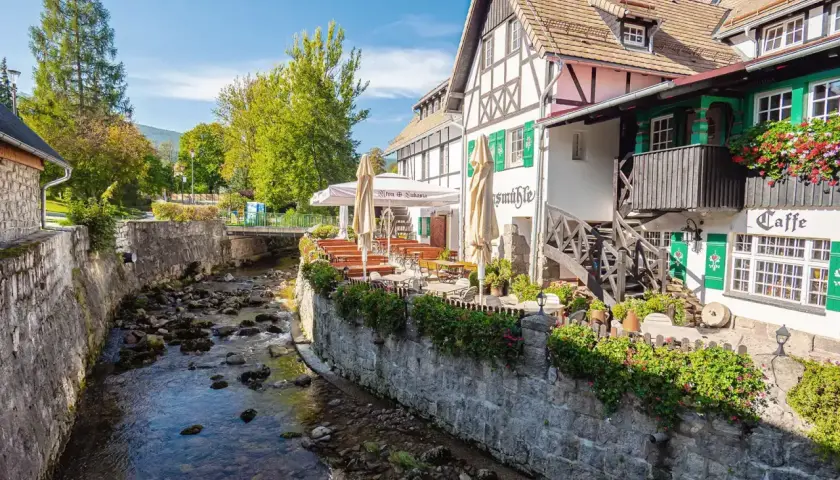 Urokliwy deptak w Szklarskiej Porębie nad kamienistym potokiem, z kawiarnią i restauracją z ogródkiem.