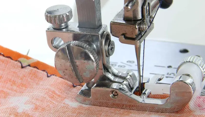 Close-up of a sewing machine needle and blind hem foot working on orange fabric. Learn how to use blind hem foot for invisible hems.